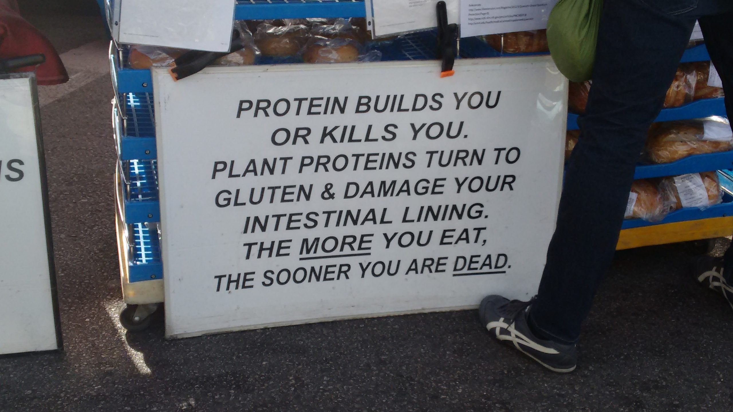Sign saying Protein builds you or kills you. Plant proteins turn to gluten & damage your intestinal lining. The more you eat, the sooner you are dead.